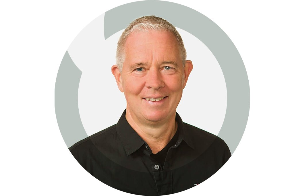 A smiling middle-aged man with short gray hair wearing a black collared shirt.