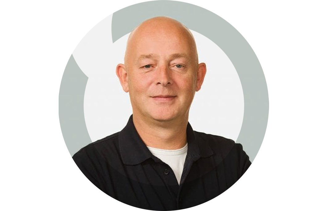 Headshot of a bald man in a black collared shirt smiling against a white background with a circular gray graphic element.